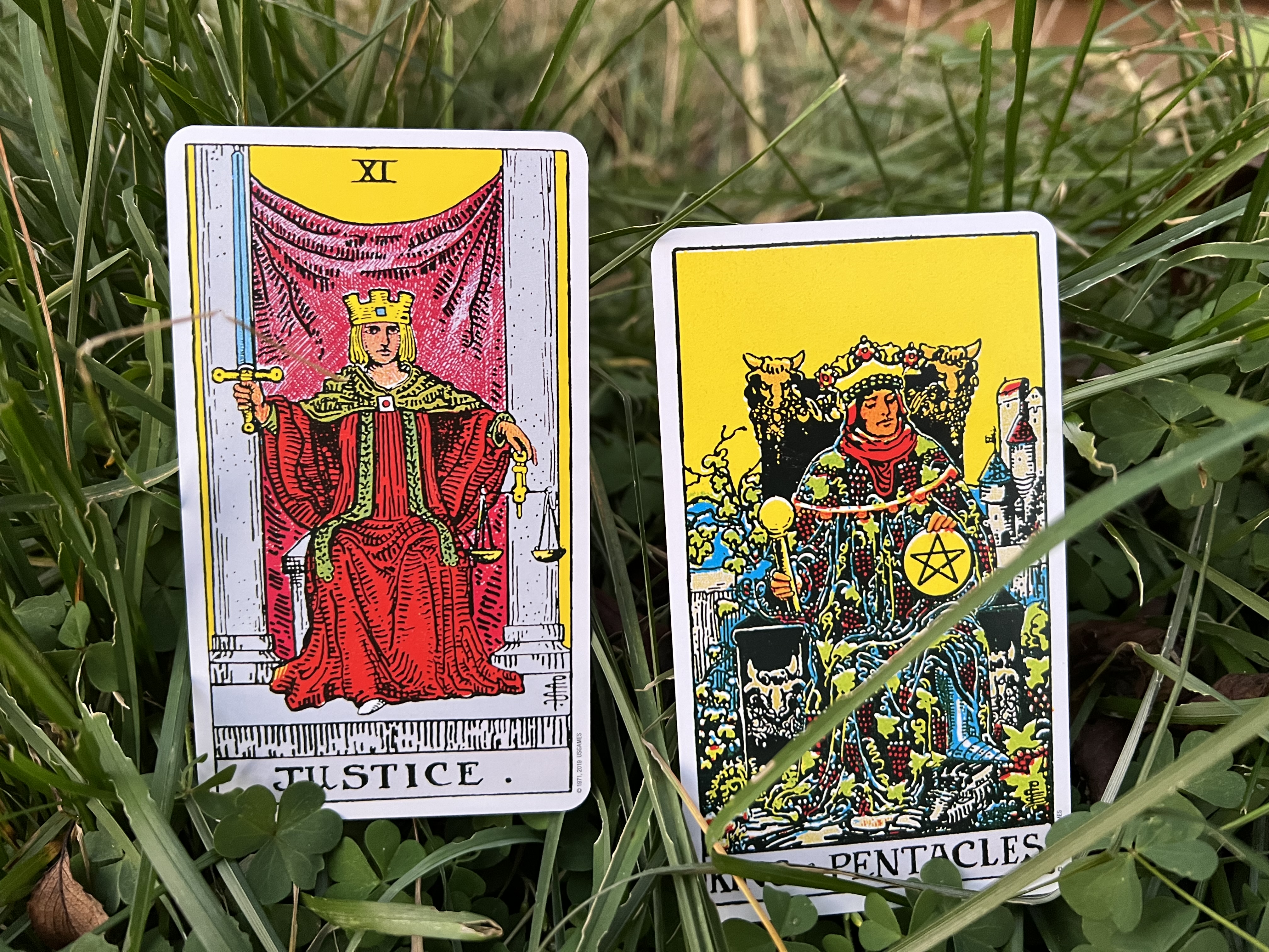 Photo of the XI Justice and the King of Pentacles cards from the Rider Waite Tarot Deck in the grass